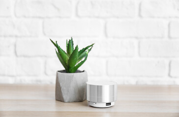 Wireless portable speaker and houseplant on wooden table near white brick wall
