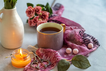 A burning candle, a cup of tea, decorative scissors, and a bouquet of flowers on a gray background. Vintage postcard. Photo