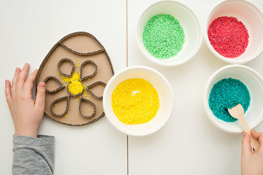 Decorating an Easter egg with colored rice. A tool for children to develop fine motor skills while playing. DIY toy for hand-eye coordination.