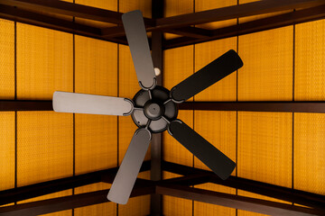 brown indoor ceiling fan on an exposed wooden support beam, with a decorate wooden ceiling, in the...