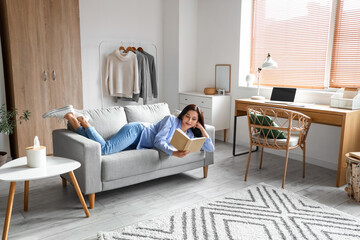 Beautiful woman with book resting on couch at home