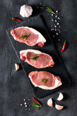 A pieces of raw fresh pork with rosemary on a cutting board on dark background. Meat with spices