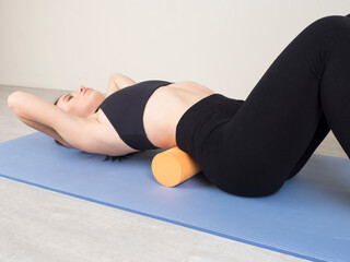 European girl is engaged in Fitness on the back. cool down after workout. independent massage of the muscles of the back and buttocks on a massage roller.