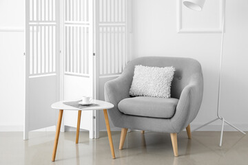 Modern table with cup, magazine and armchair in interior of light room