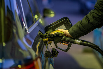 Hand of an adult man holding a gasoline pump and filling his car with petrol at gas station at night