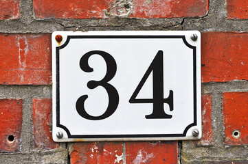 Sign of a street number 34 on a red brick wall