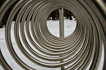 Stojak na rowery w kształcie spirali , wykonany z " nierdzewnej " stali w parku miejskim zimą na tle śniegu . Stand for spiral-shaped bikes, made of "stainless" steel in the winter park in winter on a