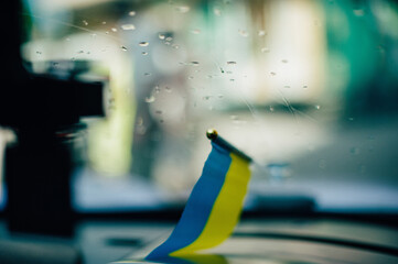 Concept of ending war in Ukraine. Ukrainian flag on glass inside car. Window with raindrops on...
