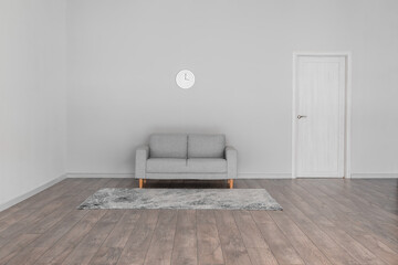 Modern sofa, carpet and clock hanging on light wall in big room