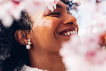 Happy woman, smiling, showing her white teeth among the pink spring flowers on a sunny morning day....