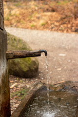 Old rustic drinking water fountain in the forest. Wooden construction, rusty metal pipe and faucet, streaming water. Close up shot, shallow depth of field, no people