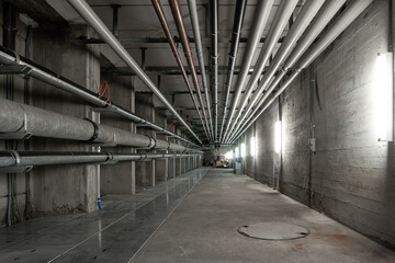 Ceiling mounted industrial pipelines inside underground  building, Long corridor with metal floors, dimly lit, no people - obrazy, fototapety, plakaty