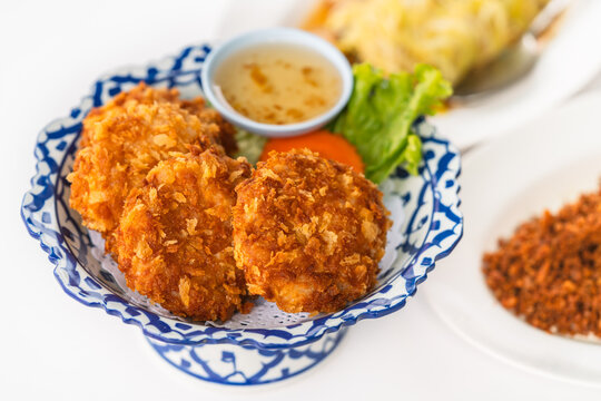 Deep-fried shrimp Cake on a beautiful plate with plum sauce, close-up image of deep-fried shrimp cake with blurred other food on white background, an image of crispy Thailand food.