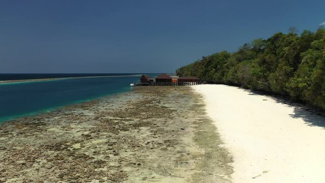 Drone approaching to a dock on a tropical island with white sand, palm trees and coral reef