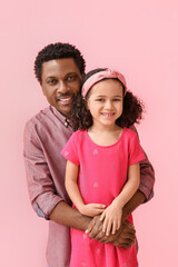 Portrait of little African-American girl and her father on pink background