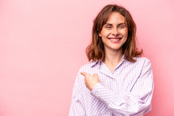 Young caucasian woman isolated on pink background smiling and pointing aside, showing something at blank space.