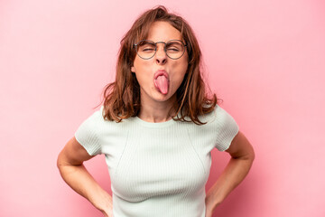 Young caucasian woman isolated on pink background funny and friendly sticking out tongue. - obrazy, fototapety, plakaty