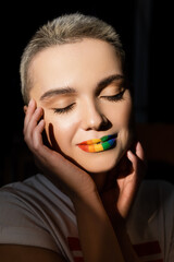 junge frau mit regenbogenfarben lippen und händen in der nähe des gesichts isoliert auf schwarz. © LIGHTFIELD STUDIOS