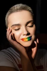 junge frau mit regenbogenfarben lippen und händen in der nähe des gesichts isoliert auf schwarz. © LIGHTFIELD STUDIOS