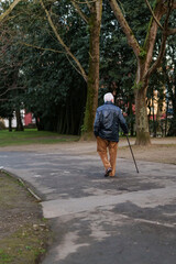 Old man with cane and jacket walking in the park