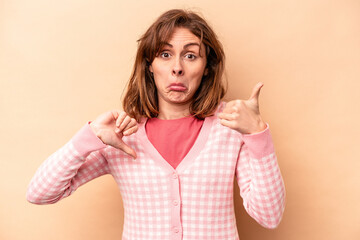 Young caucasian woman isolated on beige background showing thumbs up and thumbs down, difficult...