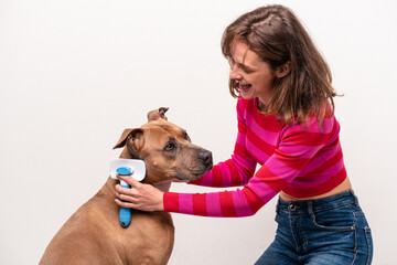 Young caucasian woman combing her dog isolated on white background