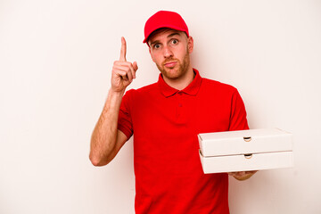 Young delivery caucasian man holding pizzas isolated on white background showing number one with finger.