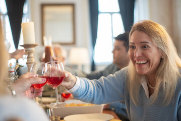 Happy mid adult woman clinking glasses at family party. Cheerful people drinking wine during family...