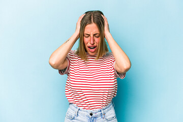 Young caucasian woman isolated on blue background covering ears with hands trying not to hear too loud sound.