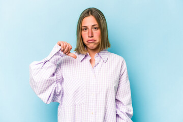 Young caucasian woman isolated on blue background showing a dislike gesture, thumbs down....