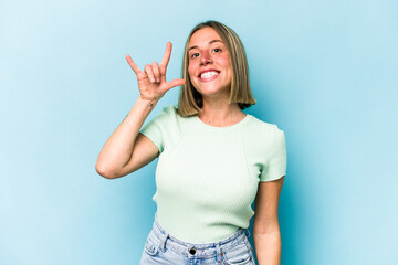 Young caucasian woman isolated on blue background showing a horns gesture as a revolution concept.