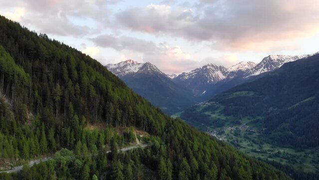 Aerial flyover along a forest road in Val d' Anniviers near St. Luc, Switzerland with a view of the peaks around Zinal and Grimentz at the end of a summer day