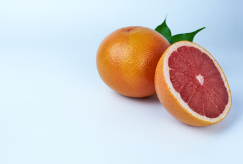a whole grapefruit and a half with green leaves on a white background