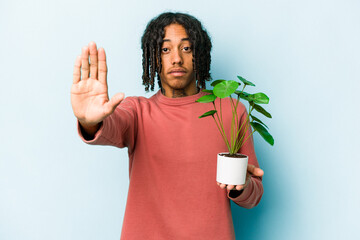 Young African American man holding a plant isolated on blue background standing with outstretched...