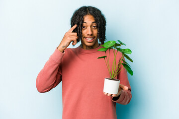 Young African American man holding a plant isolated on blue background showing a disappointment gesture with forefinger.