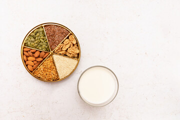 Glass of vegetable milk and a plate divided into sectors with various seeds and nuts. Concept:...