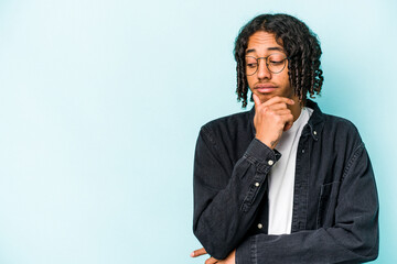 Young African American man isolated on blue background looking sideways with doubtful and skeptical expression.