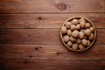 Walnuts in a shell in a wooden plate on a brown background with place for text