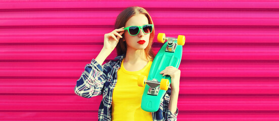 Portrait of stylish young woman model with skateboard wearing shirt, sunglasses and backpack on vivid pink background