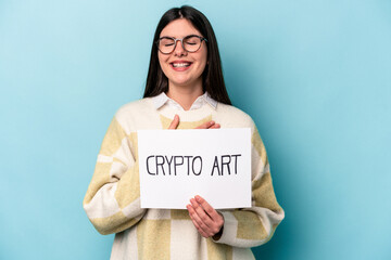 Fototapeta na wymiar Young caucasian business woman holding a crypto art placard isolated on blue background laughs out loudly keeping hand on chest.