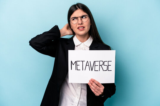 Young caucasian business woman holding a metaverse placard isolated on blue background touching back of head, thinking and making a choice.
