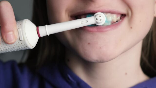 Girl brushes her teeth with an electric toothbrush with toothpaste, close up.