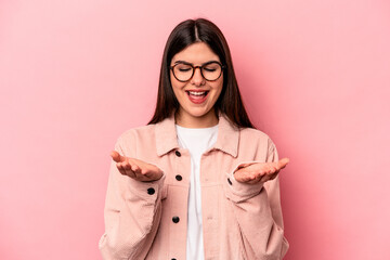 Young caucasian woman isolated on pink background holding something with palms, offering to camera.