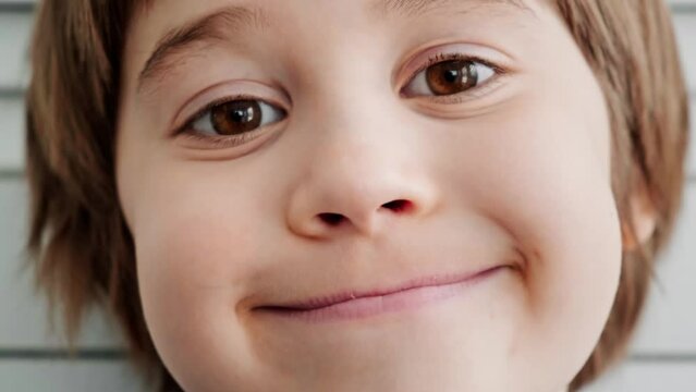 Close-up portrait of 5 year European smiling boy. Pretty face with big brown eyes. Child looking at camera. Happy mood. Kid toothless mouth. Sincere emotions. Slow motion. Childhood lifestyle concept.