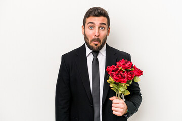 Young caucasian man holding a bouquet of flowers isolated on white background shrugs shoulders and open eyes confused.