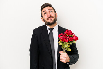 Young caucasian man holding a bouquet of flowers isolated on white background dreaming of achieving...