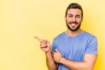 Young caucasian man isolated on yellow background smiling cheerfully pointing with forefinger away.