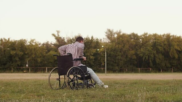 Disabled man in wheelchair on grass is miraculously healed gets up and walks forward, back view. Recovery of disabled man with paralyzed legs. Concept of miracle