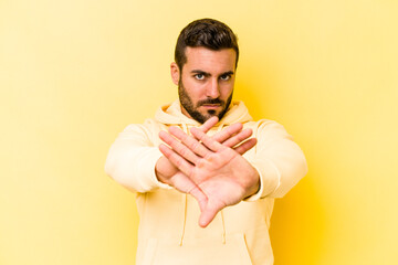 Young caucasian man isolated on yellow background standing with outstretched hand showing stop sign, preventing you.