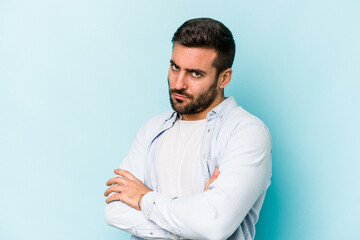 Young caucasian man isolated on blue background frowning face in displeasure, keeps arms folded.